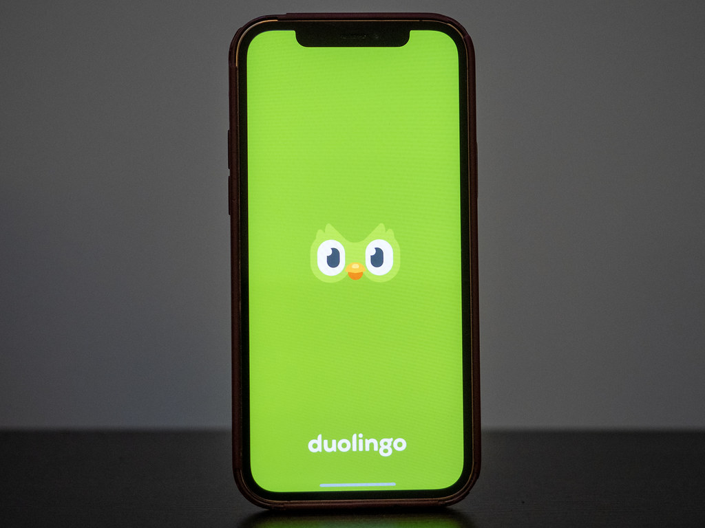 Un iPhone sobre una mesa muestra la pantalla verde de inicio de Duolingo